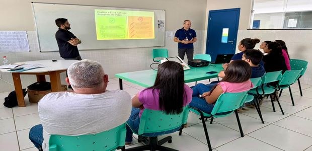Em uma sala de treinamento, um grupo de pessoas está sentado em cadeiras verdes, voltado para du...