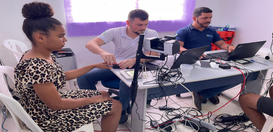 Mulher sentada tem a digital do dedo coletada por um técnico em uma mesa com equipamentos biomét...