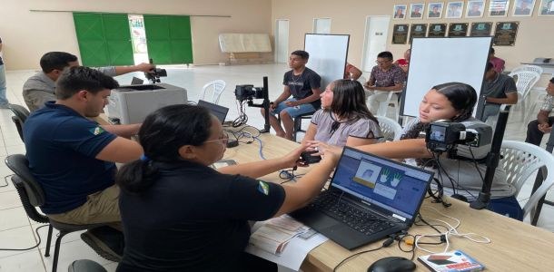 Pessoas participam de atendimento para emissão de título de eleitor. Em uma sala, servidores uti...