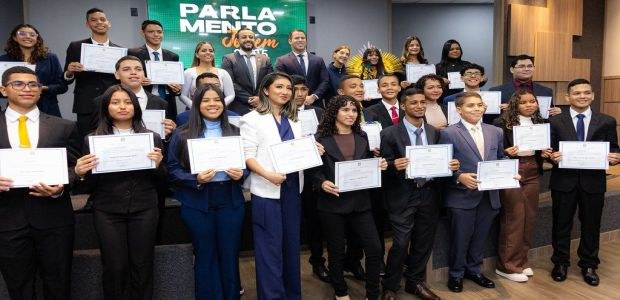 TRE-RR- Parlamento Jovem A foto mostra um grupo de jovens vestidos formalmente, em trajes sociais, posando em um auditóri...