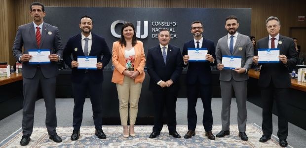 A imagem mostra um grupo de sete pessoas em pé, lado a lado. Elas estão posicionadas no centro d...