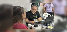 A imagem mostra um ambiente de atendimento, com uma mesa onde estão um computador portátil, vári...
