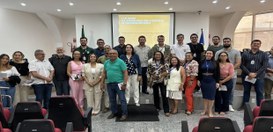 A imagem mostra um grupo grande de pessoas reunidas em um auditório. Elas estão posicionadas em ...