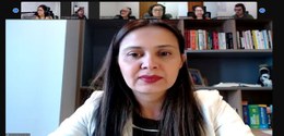 A imagem mostra uma reunião virtual. No centro, em destaque, está uma mulher de pele clara e cab...
