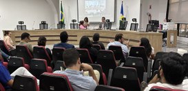 Fotografia de uma reunião realizada em um auditório. Em primeiro plano, várias pessoas estão sen...