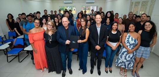 Fotografia realizada em uma sala de aula ou auditório, mostrando um grande grupo de pessoas reun...