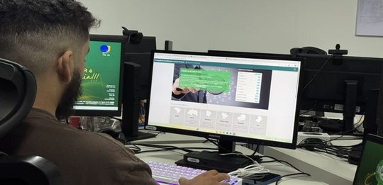 Pessoa utilizando um computador em ambiente de escritório, com duas telas de monitor à sua frent...