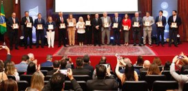 A imagem mostra um evento formal realizado em um auditório. No centro da cena, há uma fileira de...