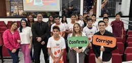 Grupo de adolescentes e adultos em sala com cadeiras vermelhas, posando para foto. Algumas pesso...