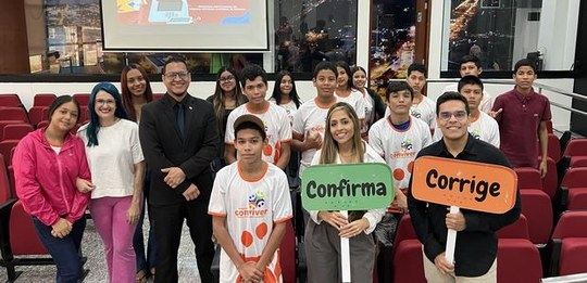 Grupo de adolescentes e adultos em sala com cadeiras vermelhas, posando para foto. Algumas pesso...