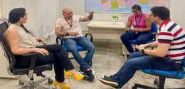 A foto mostra quatro pessoas em uma sala de reuniões simples, sentadas em cadeiras em círculo, c...