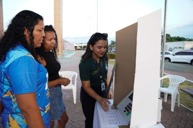 Em uma atividade pública realizada à noite, uma pessoa utiliza uma urna eletrônica posicionada s...