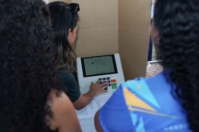 Em uma atividade pública realizada à noite, uma pessoa utiliza uma urna eletrônica posicionada s...
