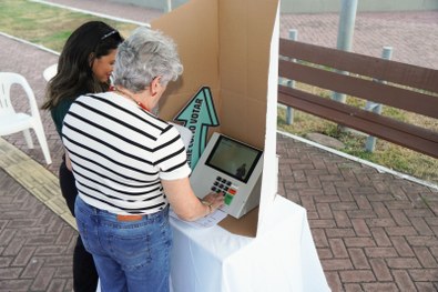 Em uma atividade pública realizada à noite, uma pessoa utiliza uma urna eletrônica posicionada s...