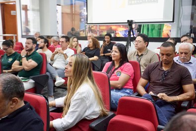 Grupo de participantes posa em um auditório, em frente a uma tela de apresentação sobre o projet...