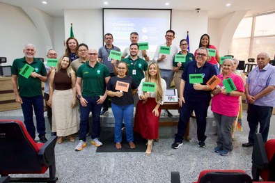 Grupo de participantes posa em um auditório, em frente a uma tela de apresentação sobre o projet...