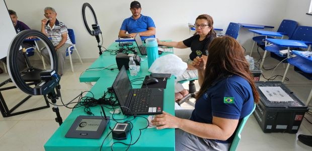 TRE-RR- Bonfim e Caracaraí recebem serviços da Justiça Eleitoral Itinerante A imagem mostra uma sala com várias pessoas envolvidas em um atendimento. Duas mulheres e um hom...
