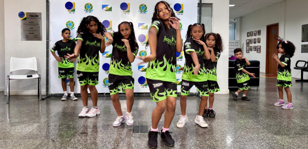 Um grupo de crianças está dançando em um espaço interno. Elas vestem roupas esportivas pretas co...