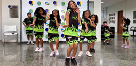 Um grupo de crianças está dançando em um espaço interno. Elas vestem roupas esportivas pretas co...