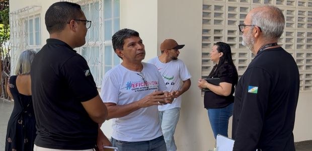 TRE-RR- Vistorias nos locais de votação Grupo de pessoas conversa em área externa ao lado de um prédio claro. Três homens estão em prime...